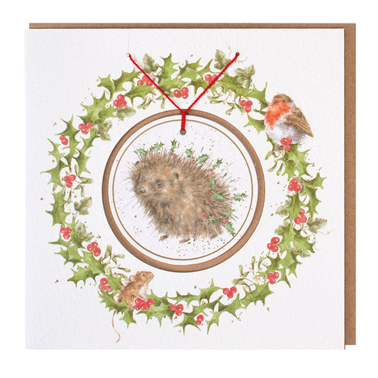 Wrendale Designs Christmas card with foiled, detachable decoration featuring Hannah Dale's artwork of a Hedgehog with Holly decorating her spines and titled <i>Hogs and Kisses</i>