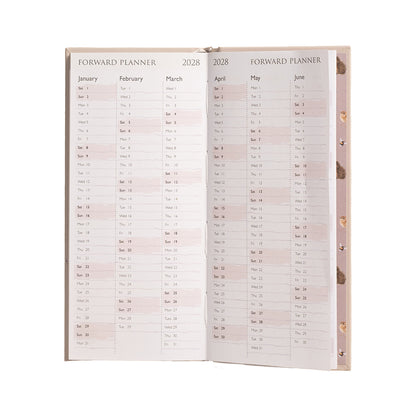 An open 2028 forward planner with two inner pages spread open, showing monthly calendar grids in black text on a pale blush-beige background. The planner has a light beige cover with gold-toned grommets visible on the right edge.